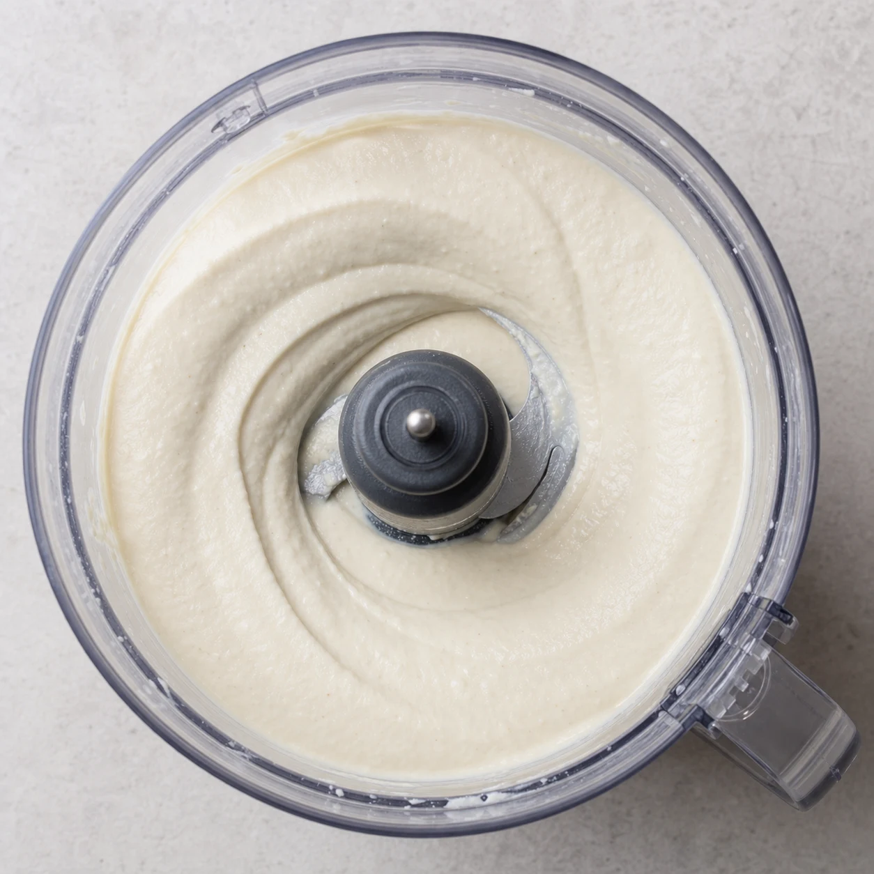 Bol de mixeur vu de près contenant une crème blanche épaisse et lisse de tofu et cajou, sans herbes ni ingrédients futurs.