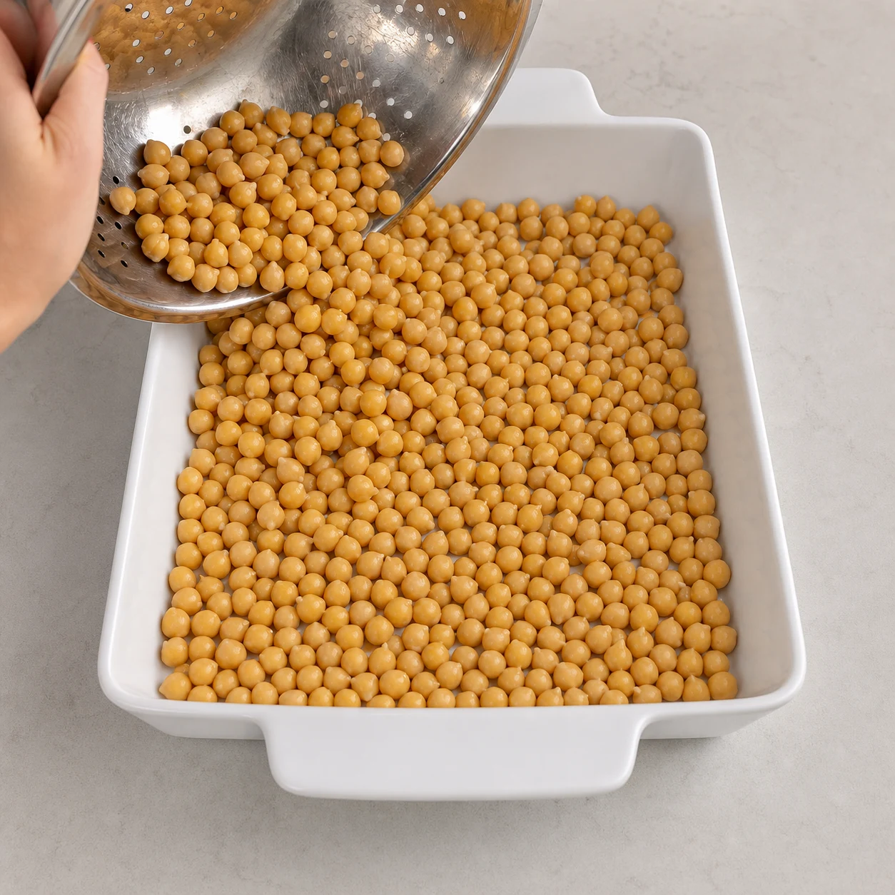 Pois chiches égouttés versés en couche régulière dans un grand plat à gratin blanc.