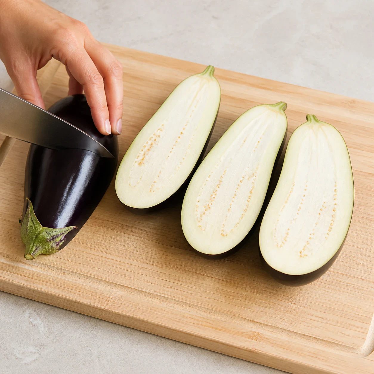 Deux aubergines violettes coupées en deux dans la longueur, quatre moitiés posées chair vers le haut sur une planche en bois claire, aucun texte, aucune marque.